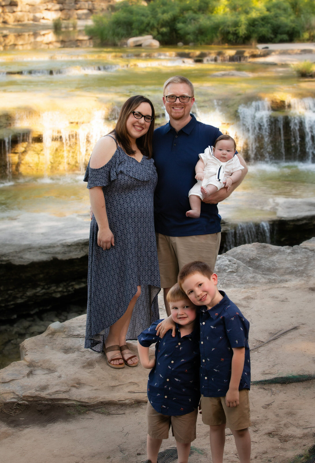 A family of five stands in front of a waterfall in matching blue outfits arlington tx pediatricians