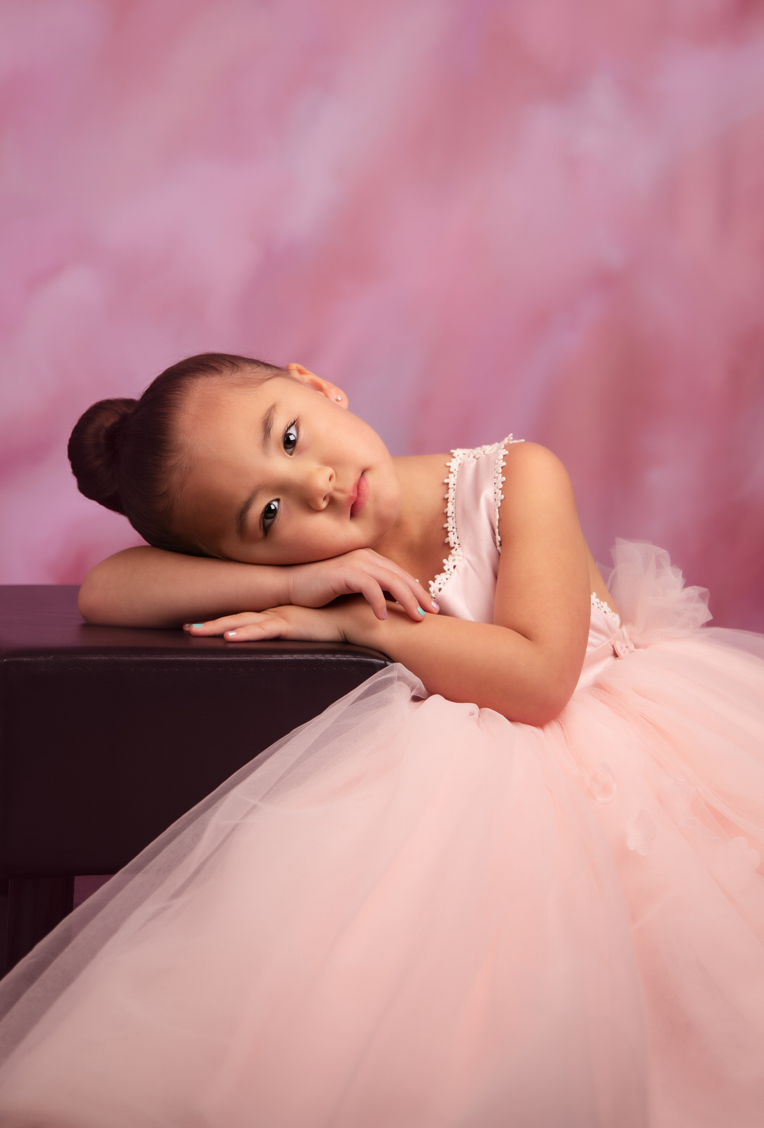 A young girl in a large tutu rests her head on a stool in a studio