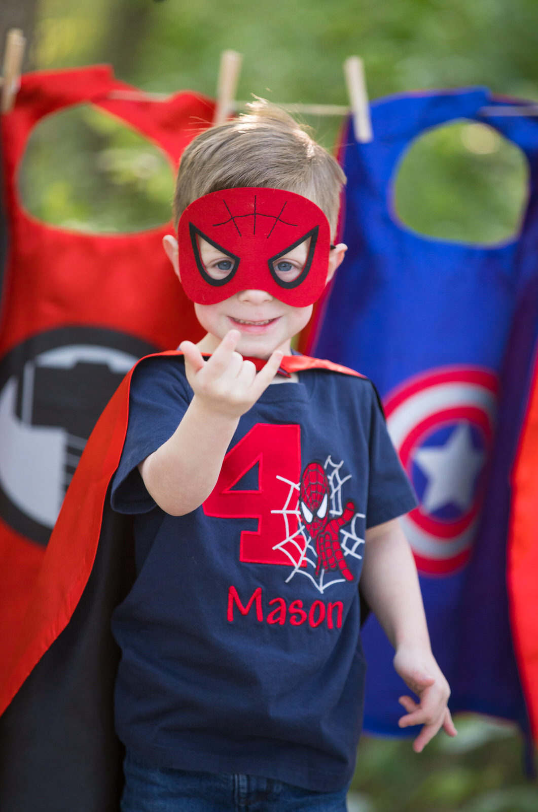 A young boy in a spiderman mask and cape makes the webbing hand in a park fort worth kids