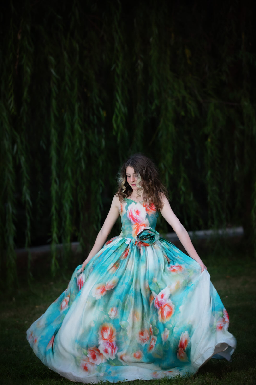 A teenage girl in a floral gown dances under a willow tree fort worth pediatricians