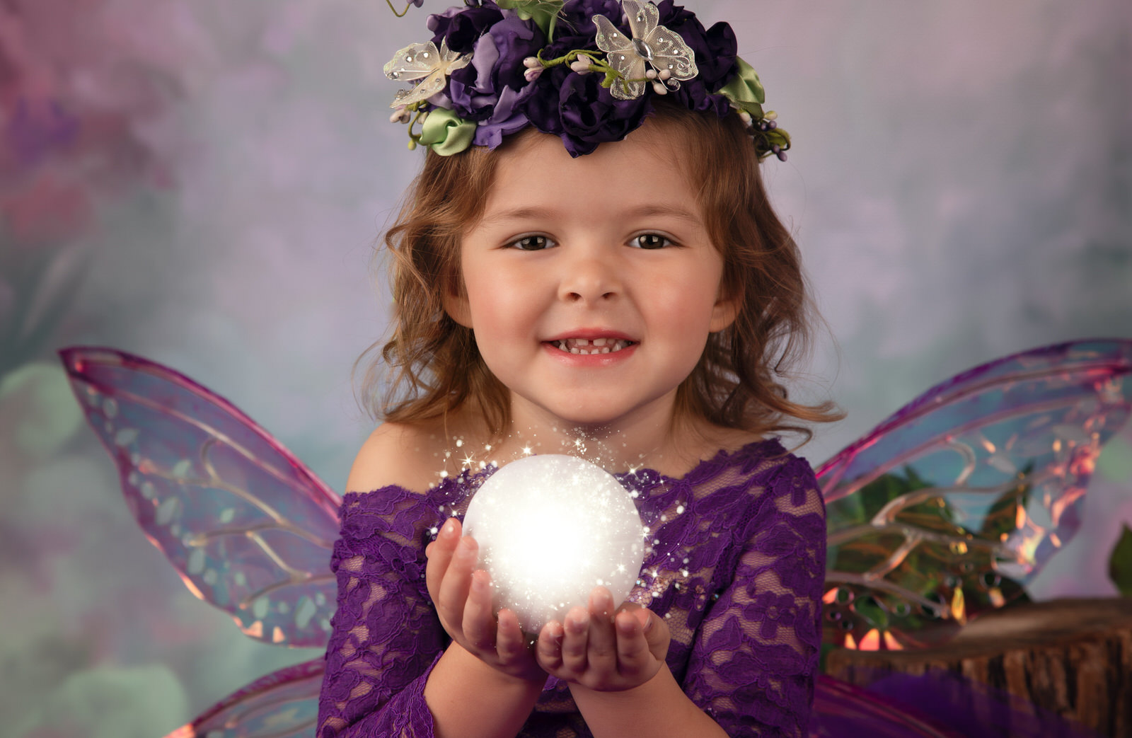 A young girl dressed as a purple fairy holds a magical orb in a studio
