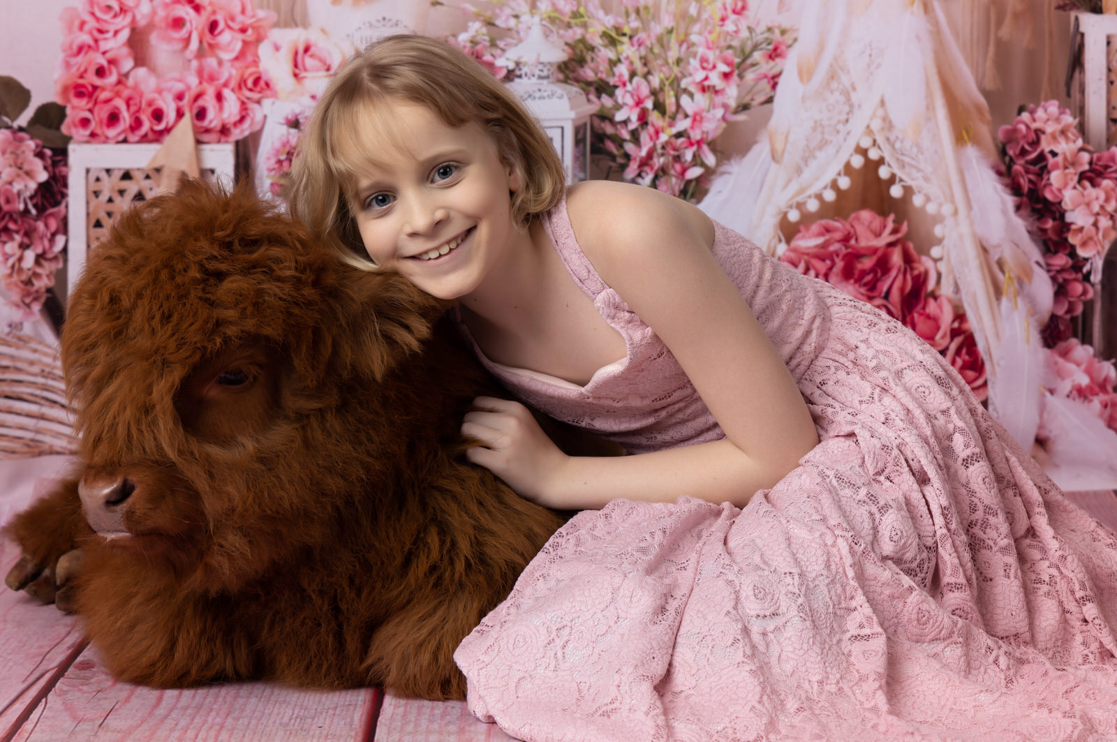 A young girl in a pink dress sits on the floor of a studio while hugging onto a baby furry cow grand prairie pediatricians