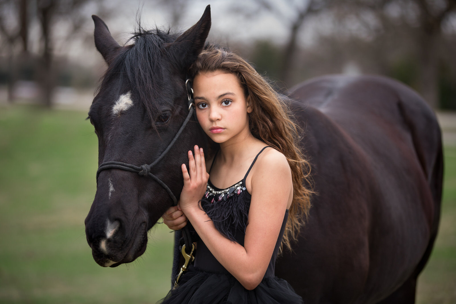 A young girl in a black dress leans against a black horse things to do in dfw with kids