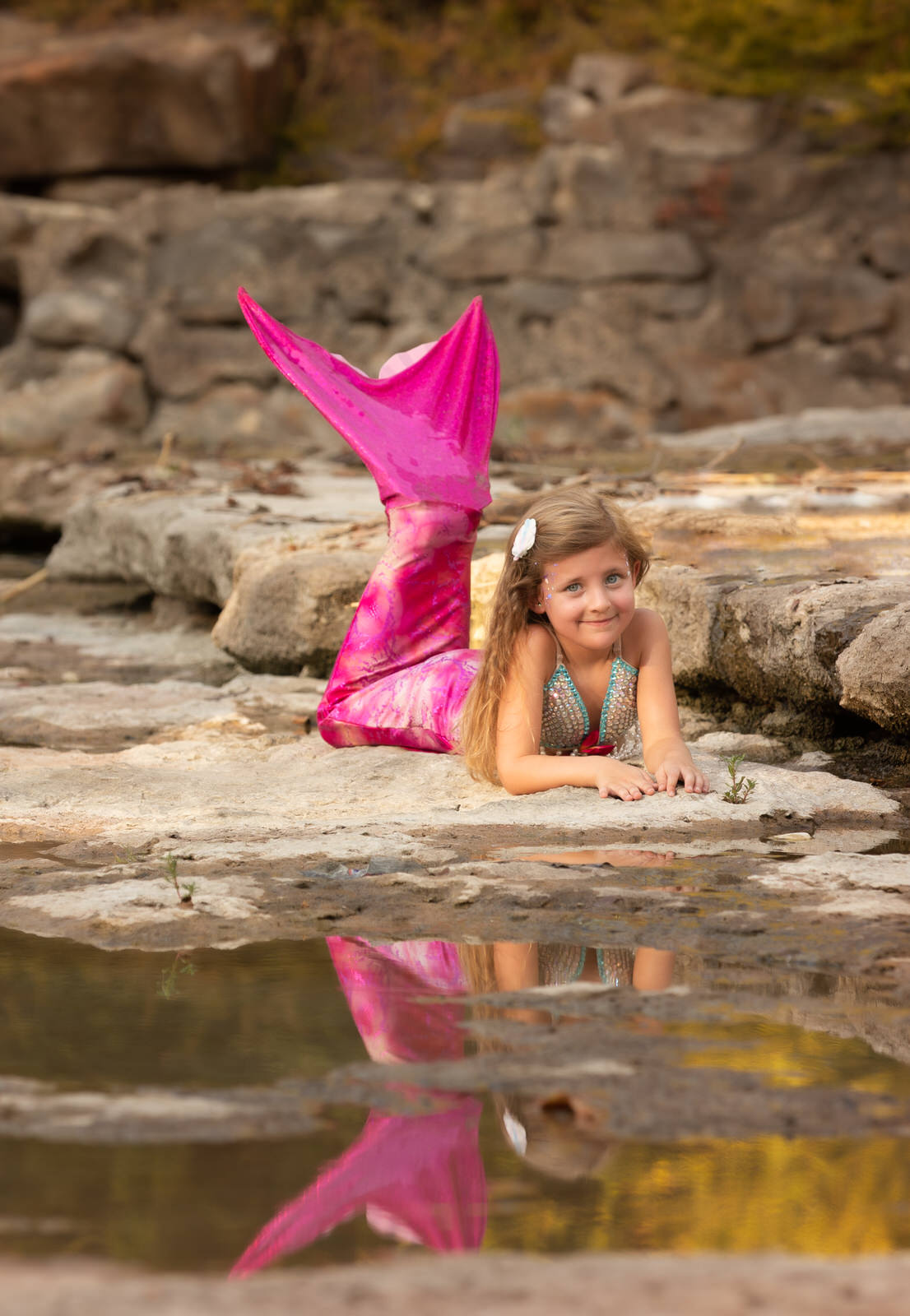 A young girl mermaid lays on the rocks of a river's edge with a pink tail things to do in grand prairie