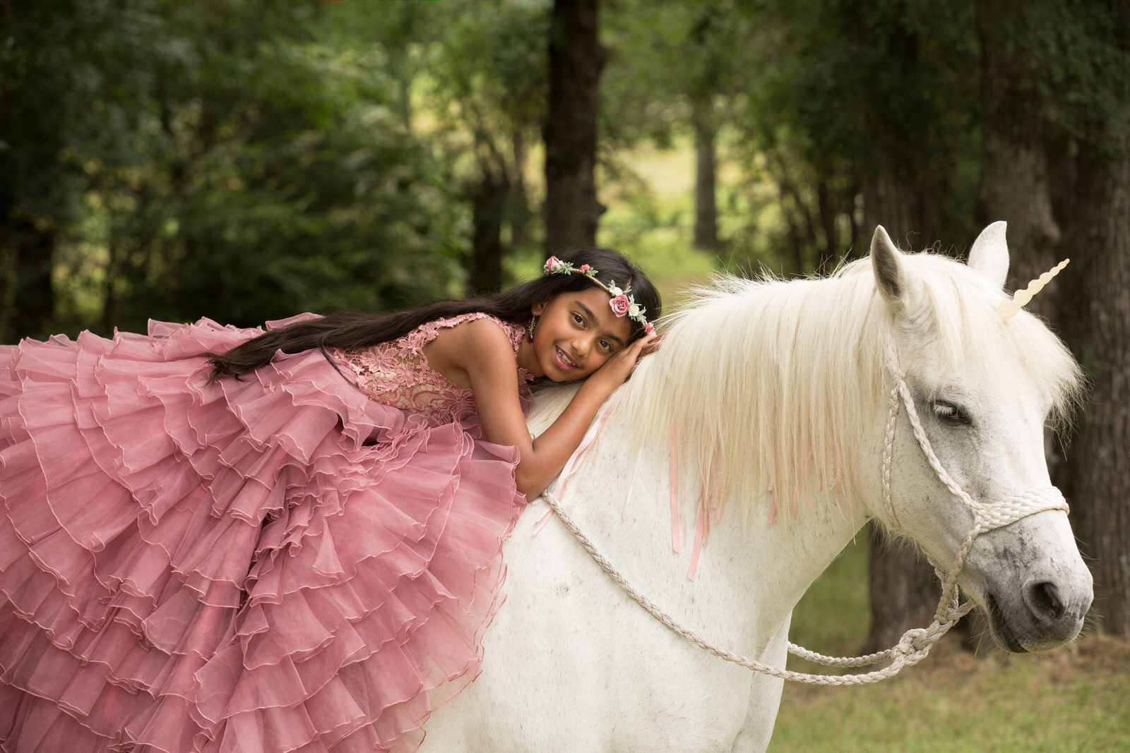 Girl in pink dress laying on a unicorn's back posing for fine art photoshoot
