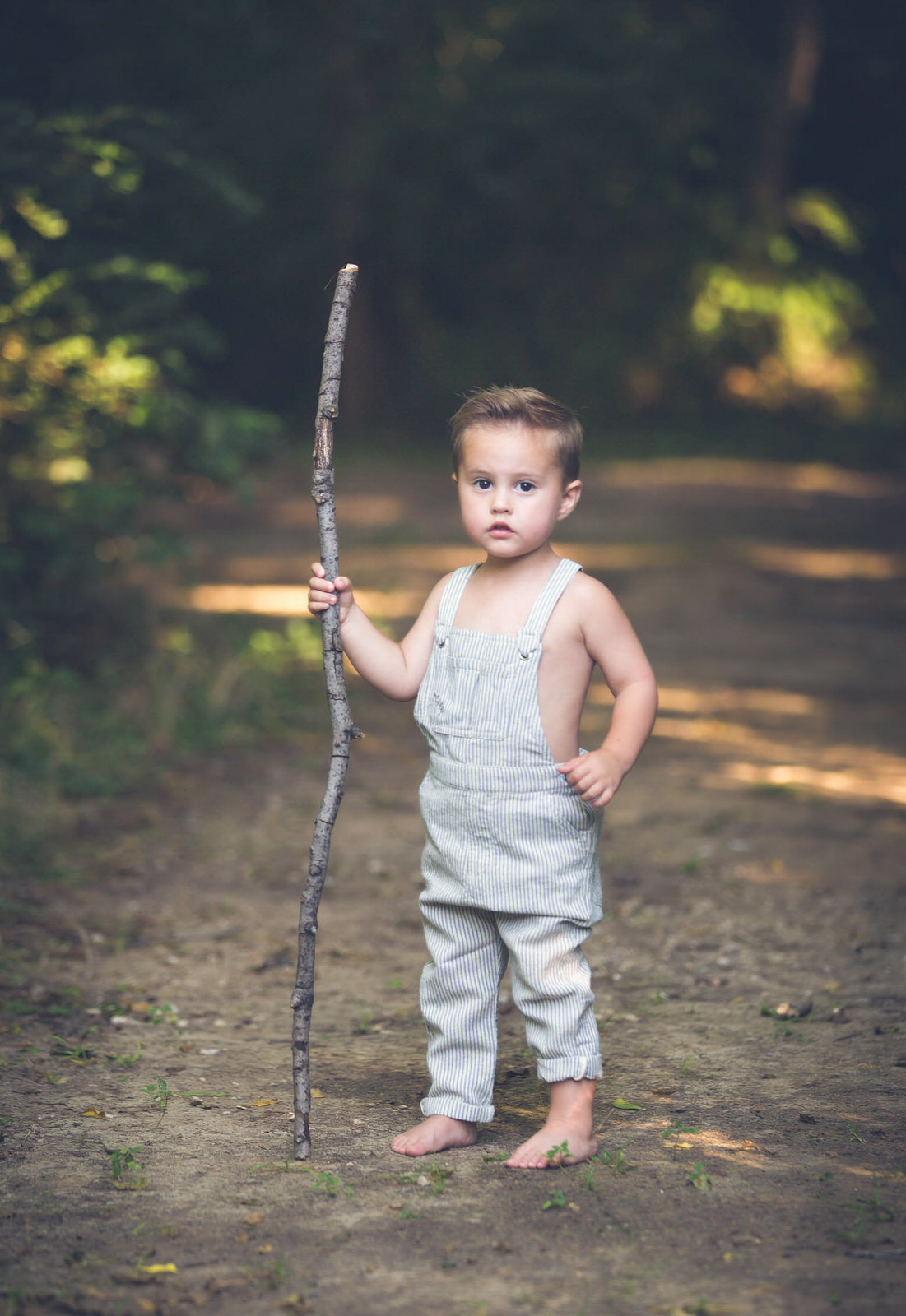 little boy in overalls holding a stick posing for Lost Boys Fishing Photography Adventure