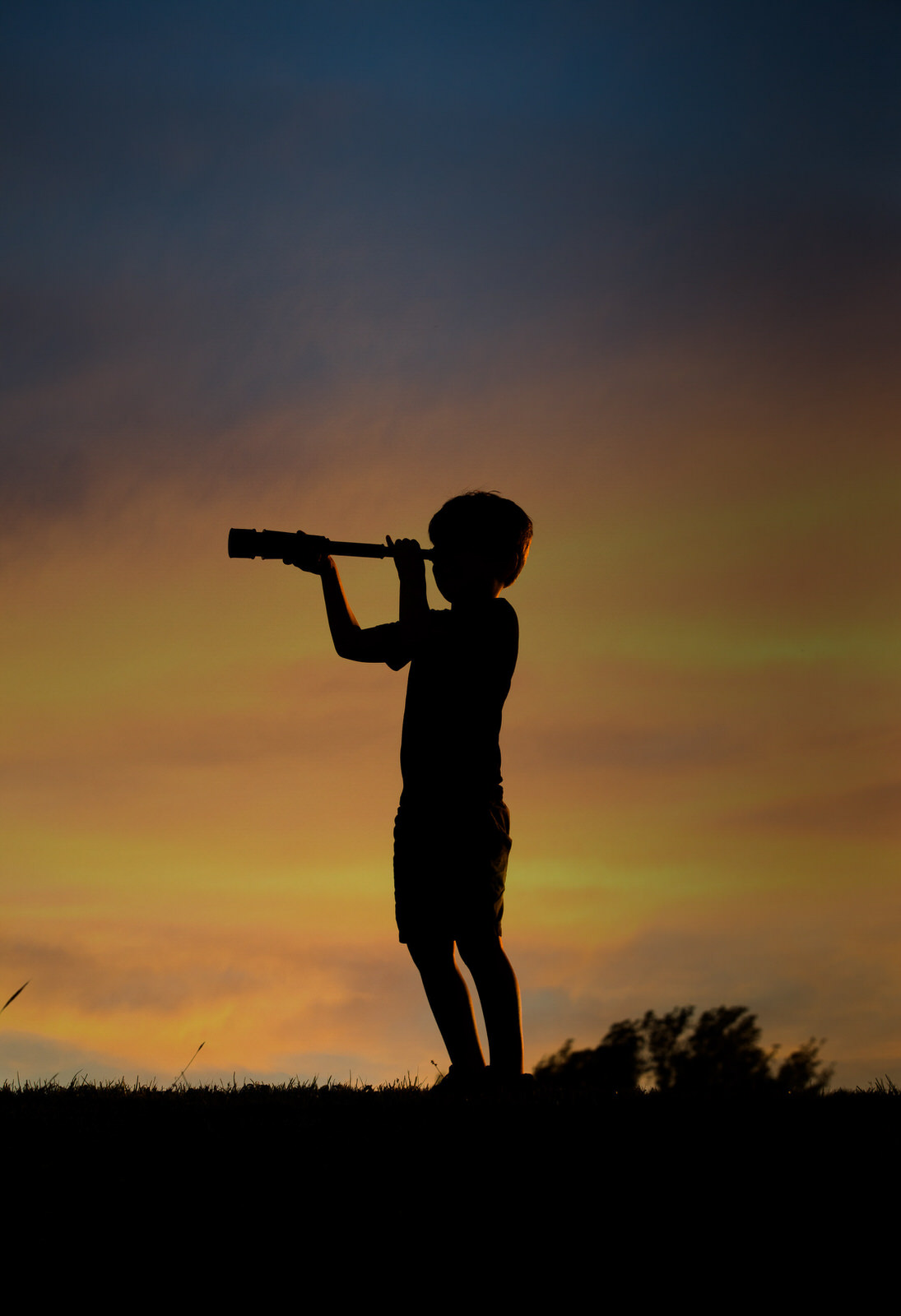 Silhouette of boy with monocular at sunset