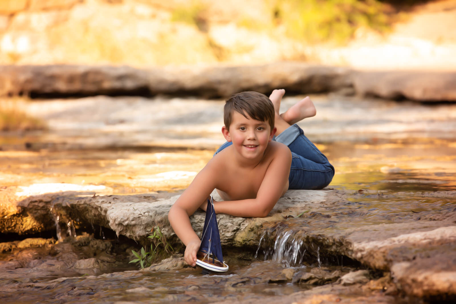 boy in creek with toy boat posing for Lost Boys Fishing Photography Adventure