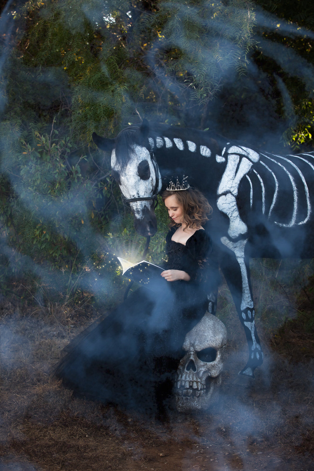 Girl in black dress sitting on skull reading to skeleton horse
